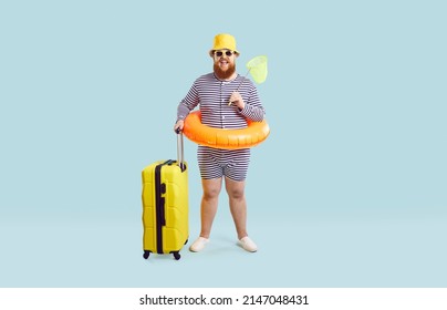 Full Body Length Of Happy Funny Fat Man In Striped Swim Suit, Hat, Glasses And Floaty Standing In Studio And Holding Yellow Suitcase And Butterfly Scoop Net. Traveling Vacation, Summer Holiday Concept