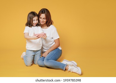 Full Body Length Happy Woman In White T-shirt Have Fun Sit Use Cell Phone Child Baby Girl 5-6 Years Old Mom Mum Little Kid Daughter Isolated On Yellow Color Background Studio Mother's Day Love Family