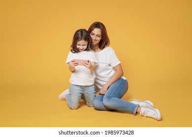 Full Body Length Happy Woman In White T-shirt Have Fun Sit Use Cell Phone Child Baby Girl 5-6 Years Old Mom Mum Little Kid Daughter Isolated On Yellow Color Background Studio Mother's Day Love Family