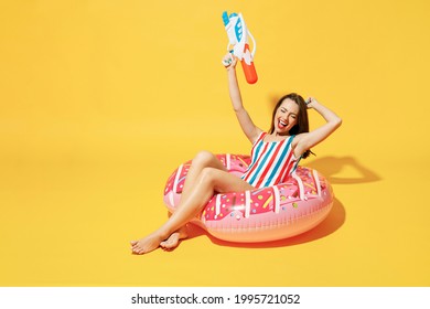 Full body length happy woman wear red blue swimsuit sit on inflatable ring hold in hand play shoot from water gun isolated on yellow color background studio Summer hotel pool sea rest sun tan concept