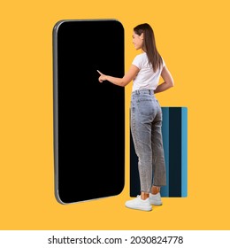 Full Body Length Of Happy Woman Touching Display Of Big Smartphone With Blank Black Screen And Credit Card, Cheerful Lady Using App Or Website, Paying Online, Standing On Yellow Background, Mock Up - Shutterstock ID 2030824778