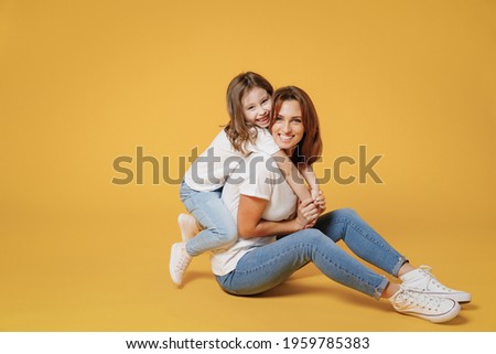 Full body length happy woman in basic white t-shirt have fun sit on floor child baby girl 5-6 years old Mom mum little kid daughter isolated on yellow color background studio Mother's Day love family