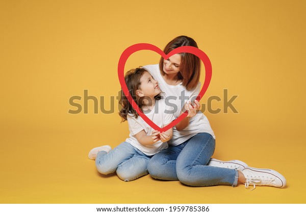 Full body length happy woman in basic white\
t-shirt have fun sit on floor child baby girl 5-6 years old Mom mum\
little kid daughter isolated on yellow color background studio\
Mother\'s Day love family