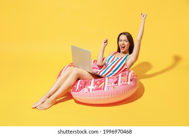 Full body length happy young sexy woman wear red blue swimsuit sit on inflatable ring work on pc laptop isolated on vivid yellow color wall background studio Summer hotel pool sea rest sun tan concept