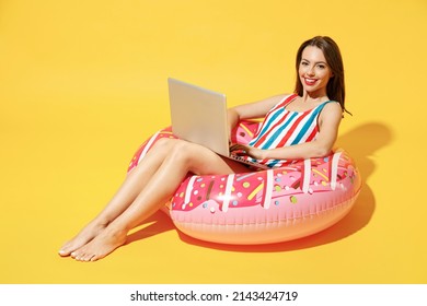 Full body length happy young sexy woman wear red blue swimsuit sit on inflatable ring work on pc laptop isolated on vivid yellow color wall background studio Summer hotel pool sea rest sun tan concept