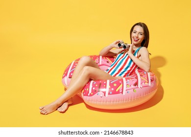 Full body length happy young woman wear red blue swimsuit sit on inflatable ring look through binocular isolated on vivid yellow color wall background studio Summer hotel pool sea rest sun tan concept