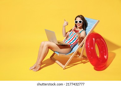 Full body length happy young woman wear red blue one-piece swimsuit sit on chair work hold laptop pc isolated over vivid yellow color wall background studio. Summer hotel pool sea rest sun tan concept - Powered by Shutterstock