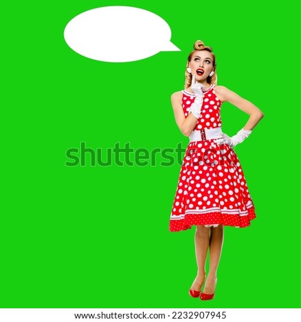 Full body length image of thinking woman in red pin up dress. Blond pinup thougthfull girl in studio, on green chroma key background. Empty blank speech sign bubble, having idea.