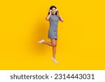 Full body length photo of korean beautiful girl new sony headphones quality music jumping wear striped dress isolated on yellow background