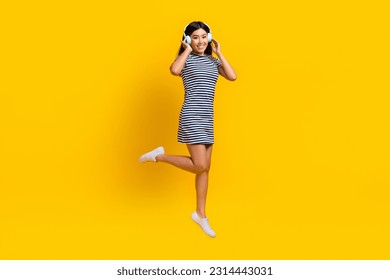 Foto de cuerpo completo de la hermosa joven coreana auriculares nuevos sony de calidad música saltar vestido a rayas aislado en fondo amarillo
