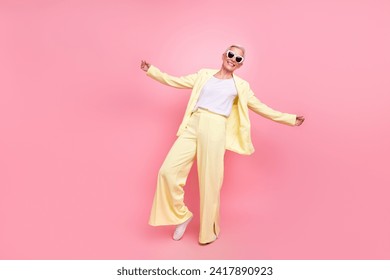 Full body length photo of satisfied woman dress relaxed fit yellow suit posing dance in sunglasses isolated on pink color background - Powered by Shutterstock