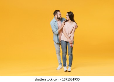 Full body length smiling young couple two friends man woman in pastel blue casual clothes hugging standing looking to each other isolated on yellow wall background studio portrait. Mock up copy space
