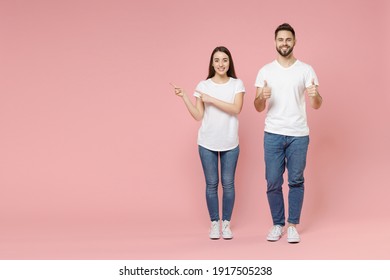 Full Body Length Young Cheerful Couple Two Friends Man Woman In White Basic Blank Print Design T-shirts Jeans Standing Pointing Aside Workspace Isolated On Pastel Pink Color Background Studio Portrait