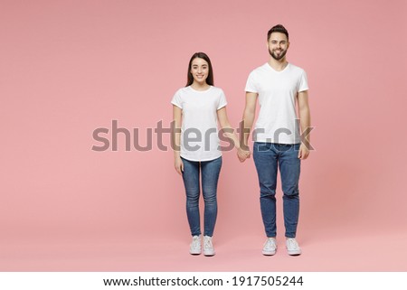 Full body length young cheerful couple two friends bearded man brunette woman in white basic blank print design t-shirts jeans standing posing isolated on pastel pink color background studio portrait