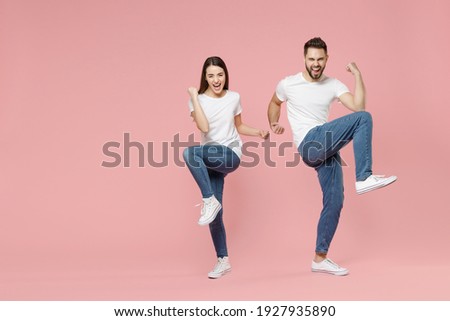 Full body length young cheerful fun couple two friends bearded man brunette woman in white basic blank print design t-shirts jeans celebrating isolated on pastel pink color background studio portrait