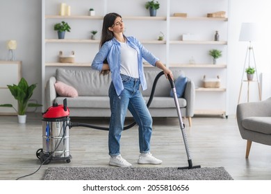 Full Body Length Of Young Exhausted Lady Having Back Ache From Cleaning Her Apartment, Vacuuming Rug Carpet In Living Room, Free Copy Space. Tired Maid Suffering From Pain Cleaning Dirty House