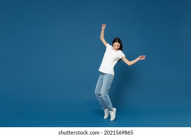 Full body length young latin woman 20s in white casual basic t-shirt keep hands outstretched leaning back look aside standing on toes dancing have fun isolated on dark blue background studio portrait