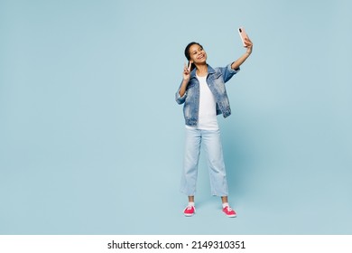 Full body little kid teen girl of African American ethnicity 12-13 years old in denim jacket do selfie shot on mobile cell phone show v-sign isolated on plain light blue background. Childhood concept - Powered by Shutterstock