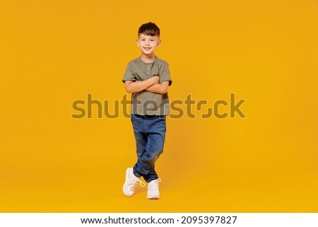 Full body little small smiling happy boy 6-7 years old wearing green t-shirt hod hands crossed folded look camera isolated on plain yellow background studio Mother's Day love family lifestyle concept