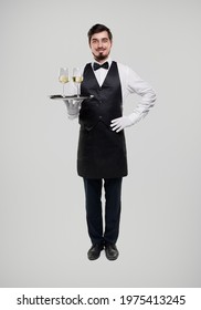 Full Body Man In Waiter Uniform Holding Hand On Waist And Carrying Tray With Goblets Of Champagne Against Gray Background