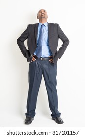 Full Body Mature Indian Business Man Hand On Waist And Looking Up, Standing On Plain Background.