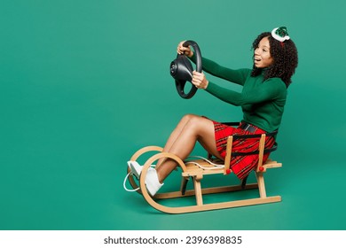 Full body merry little kid teen girl wear hat casual clothes posing sledding hold steering wheel driving car isolated on plain green background. Happy New Year celebration Christmas holiday concept - Shutterstock ID 2396398835