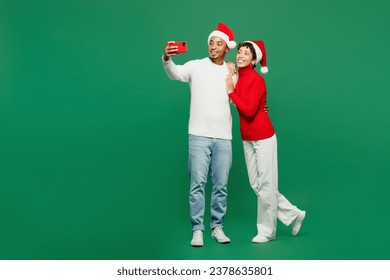 Full body merry young couple man woman wear red casual clothes Santa hat posing doing selfie shot on mobile cell phone isolated on plain green background. Happy New Year 2024 Christmas holiday concept - Powered by Shutterstock