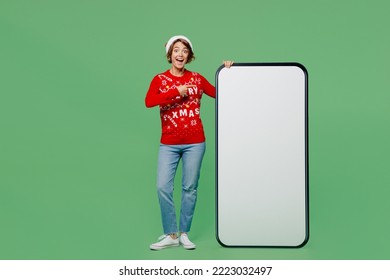 Full body merry young woman wear xmas sweater Santa hat posing point finger on big huge blank screen mobile cell phone with area isolated on plain pastel green background. Happy New Year 2023 concept - Powered by Shutterstock