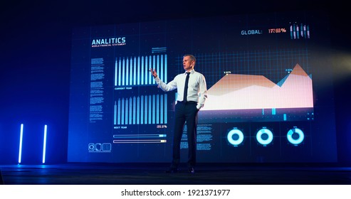 Full Body Middle Aged Speaker Holding Hand In Pocket And Talking While Standing On Stage Against LED Screen With Business Charts