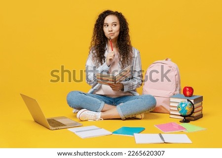 Full body minded young black teen girl student she wearing casual clothes backpack bag holding books sitting on floor isolated on plain yellow color background. High school university college concept