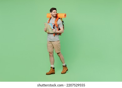Full body mountaineer young traveler white man carry backpack stuff mat walk read map look aside isolated on plain green background. Tourist leads active lifestyle Hiking trek rest travel trip concept