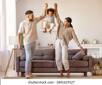 Full body multiethnic father and mother smiling and lifting mixed race son near couch in cozy living room - Shutterstock ID 1841619127