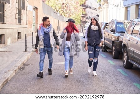 Full body of multiethnic male and female friends in stylish casual wear walking on asphalt road past cars and having conversation