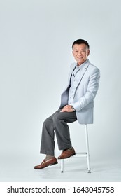 Full Body Of An Old Asian Man Wear Light Grey Suit Sitting On A Grey Chair In Studio White Background. Isolated Picture Of Happiness Asian Old Man.