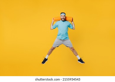 Full Body Overjoyed Excited Happy Young Fitness Trainer Instructor Sporty Man Sportsman Wear Headband Blue T-shirt Hold Yoga Mat Jump High Isolated On Plain Yellow Background. Workout Sport Concept.