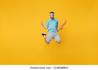 Full Body Overjoyed Young Fitness Trainer Instructor Sporty Man Sportsman In Headband Blue T-shirt Hold Yoga Mat Jump High Do Winner Gesture Isolated On Plain Yellow Background. Workout Sport Concept.