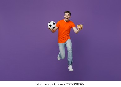 Full Body Overjoyed Young Fun Fan Man He Wearing Orange T-shirt Cheer Up Support Football Sport Team Hold In Hand Soccer Ball Chips Snack Watch Tv Live Stream Isolated On Plain Dark Purple Background