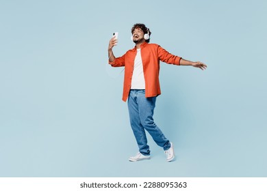 Full body overjoyed young fun Indian man wears orange red shirt white t-shirt headphones listen to music use mobile phone isolated on plain pastel light blue cyan background studio. Lifestyle concept - Shutterstock ID 2288095363
