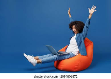 Full body overjoyed young smiling student happy black woman in casual clothes shirt white tshirt sit in bag chair hold use work on laptop pc computer finish job isolated on plain dark blue background. - Shutterstock ID 2094806872