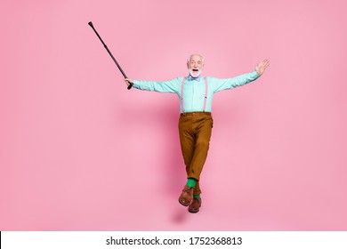 Full Body Photo Of Active Grandpa Moving Dance Senior Party Raise Up Walk Stick Leg Wear Mint Shirt Suspenders Bow Tie Pants Shoes Green Socks Isolated Pink Pastel Background