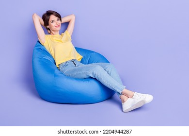 Full body photo of adorable satisfied lady sit comfy bag arms behind head isolated on violet color background