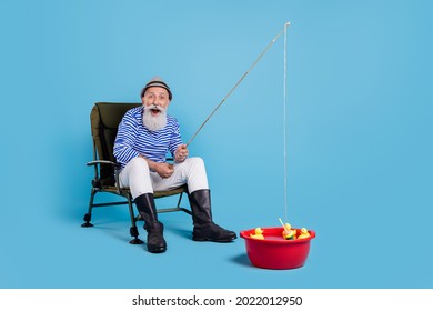 Full body photo of amazed grey haired happy old man sit chair fish basin enjoy isolated on blue color background