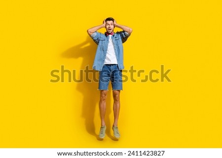 Full body photo of astonished speechless man dressed denim shirt fly arms on head staring at discount isolated on yellow color background