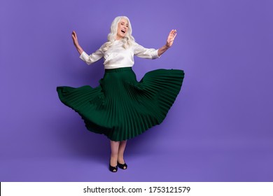Full body photo of attractive mature grey haired lady dancing retro party raise hands modern movement excited wear white blouse green long skirt flying isolated purple color background