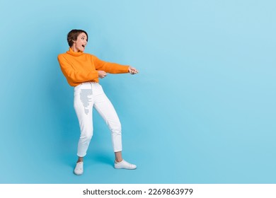 Full body photo of attractive young woman pulling rope heavy try hard impressed wear trendy orange outfit isolated on blue color background - Powered by Shutterstock