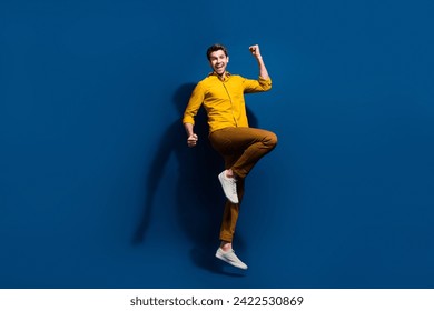 Full body photo of attractive young guy raise fists celebrate dressed stylish yellow clothes isolated on dark blue color background