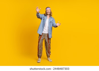 Full body photo of attractive young hippie man stretch hands hold empty space wear trendy denim outfit isolated on yellow color background - Powered by Shutterstock