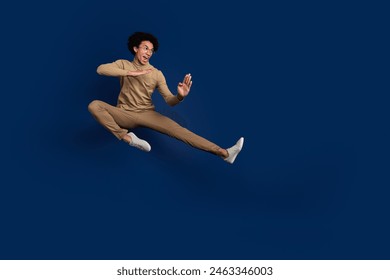 Full body photo of attractive young man fly kick karate dressed stylish beige clothes isolated on dark blue color background