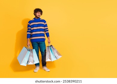 Full body photo of attractive young man hold shopping bags moody dressed stylish blue striped clothes isolated on yellow color background - Powered by Shutterstock