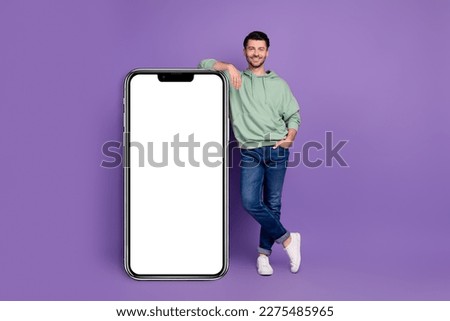 Full body photo of attractive young man leaning vertical white banner gadget dressed stylish khaki look isolated on purple color background